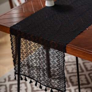 Detail of black hollow crochet table runner with wavy patterns and elegant fringe tassels