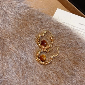 Créoles en œil de tigre avec pièces dorées texturées sur fond en peluche marron