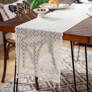 Detail of white lace table runner with geometric hollow weave and short tassels on wood table