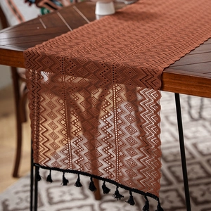 Macro detail of brown hollow lace table runner with intricate weaving and black tassels