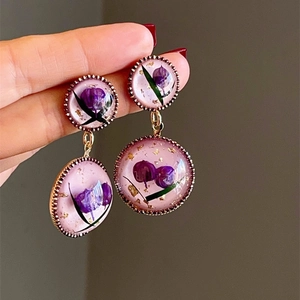 Detail view of handmade gold earrings featuring purple dried flowers and gold foil accents