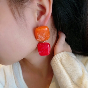 Detail of geometric resin earrings in orange and red marble texture on model