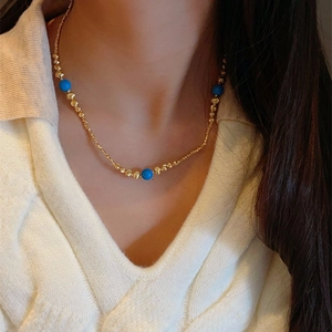 Elegant gold beaded necklace with blue stone spheres worn by a model in close-up shot