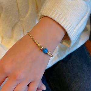 Handmade beaded bracelet with gold metal beads and a blue turquoise stone on a woman's wrist