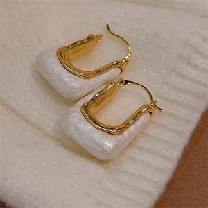 Detailed macro view of 18K gold plated U-shaped earrings on textured white knit fabric