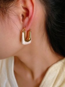Macro view of 18K gold U-shape earrings with white textured rock inlay on a model