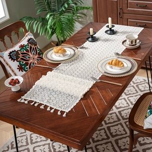 Elegant cream knit table runner with geometric lace patterns and fringe on a wooden table