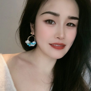 Detail of ethnic round gold earrings with white flowers and turquoise beads on model