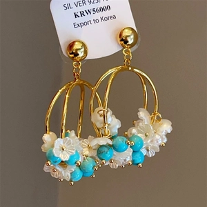 Detail of gold hollow hoops with white floral accents and turquoise beads on a 925 silver post