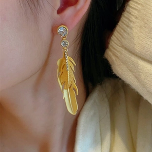 Detail of bohemian gold feather earrings with sparkling crystals worn by a model