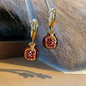 Creative pomegranate drop earrings with red crystals and gold finish on plush fabric
