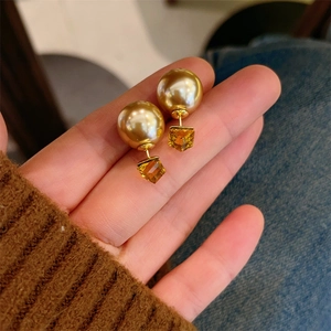 Macro detail of French style gold pearl stud earrings with amber cube pendant on hand