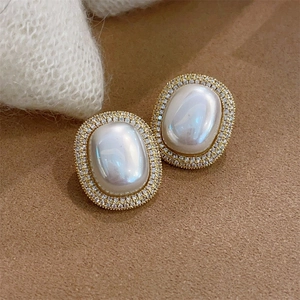 Close-up of golden oval stud earrings with white pearl and sparkling rhinestones