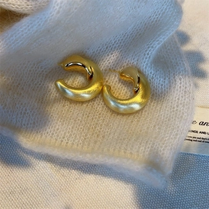 Orecchini a cerchio a forma di C in oro opaco presentati su un morbido maglione bianco