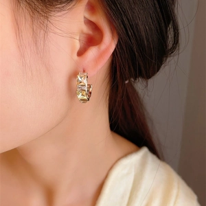 Close-up of golden C-shaped hoop earrings with square-cut crystals on a model