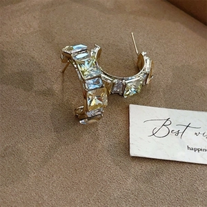 Detail of C-shaped gold earrings with square crystal stones on brown velvet background