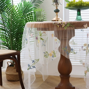 Elegant white mesh tablecloth with colorful floral and butterfly embroidery on a wooden table