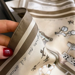 Gros plan du foulard en soie aux tons champagne, motif calèche et détails d'ourlets roulés