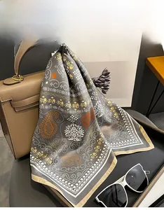 Detailed shot of grey silk scarf with gold elephant print draped over a luxury leather handbag