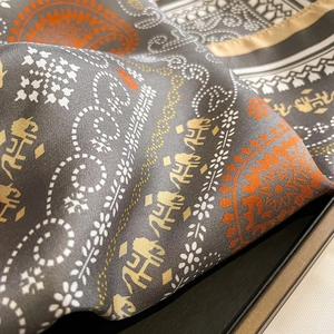 Detail of silk twill scarf with orange paisley and small elephant print on dark grey fabric