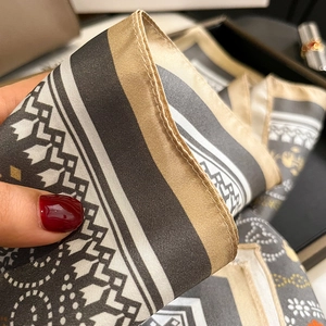 Macro detail of silk twill scarf showing refined rolled edges and geometric print patterns