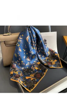Close-up of luxury dark blue silk scarf with gold bird and floral prints on a textured surface