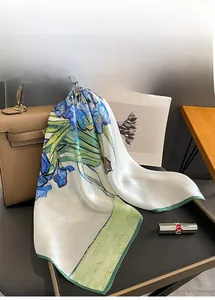 Artistic silk square scarf with blue iris print draped on a leather designer handbag