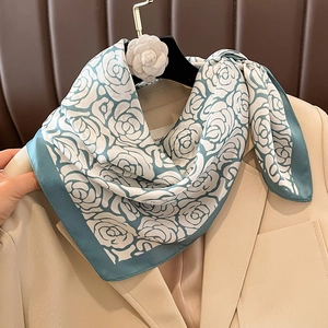 Detail of silk square scarf with green borders and rose print on a beige suit jacket