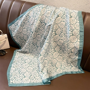 Detail of silk square scarf with green rose floral print draped on a leather sofa