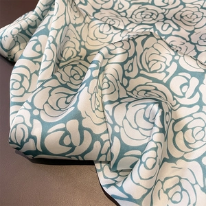 Detail of rose print silk scarf fabric with light cyan floral patterns on cream base