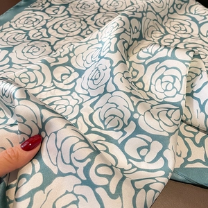 Detail showing high-gloss silk fabric with large turquoise rose prints and rolled edges