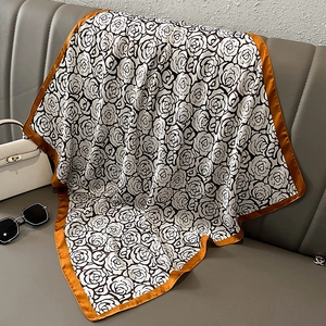 Silk scarf with black and white rose floral print and orange borders on leather sofa
