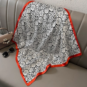 Elegant silk scarf with black and white rose pattern and red contrast border on a sofa