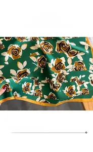 Vue détaillée du foulard en soie émeraude avec motifs de roses dorées et bord cousu
