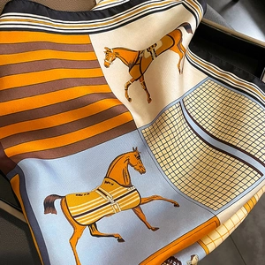 Close-up of silk square scarf featuring equestrian patterns and vibrant orange accents
