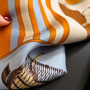 Close-up of orange and blue twill silk scarf showing elegant equestrian illustrations