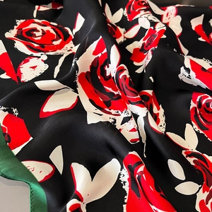 Détail d'un foulard en soie montrant des roses rouges sur tissu noir et bords verts