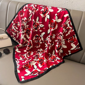 Détail d'un foulard en soie à motif rose rouge drapé sur un canapé avec accessoires