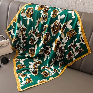 Détail d'un élégant foulard en soie verte à imprimé rose drapé sur un canapé avec accessoires