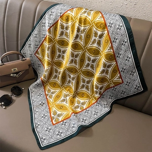 Silk-textured square scarf with gold geometric patterns styled on a brown leather sofa