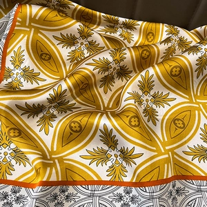 Close-up of silk scarf with yellow Baroque prints and smooth satin texture on leather