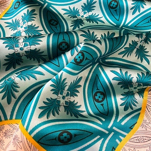 Close-up of geometric pattern silk scarf with teal and yellow edges and silky texture