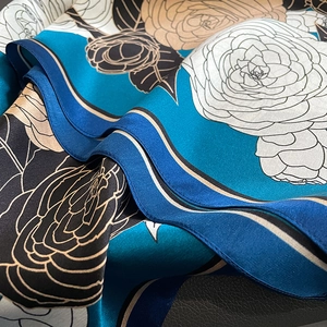 Macro shot of large floral patterns on premium glossy silk scarf with peacock blue and gold