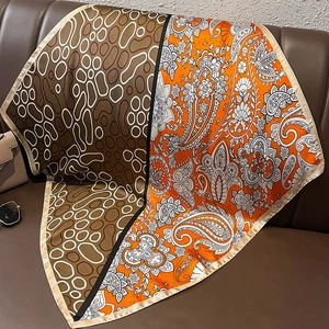 Close-up of a stylish square silk scarf with paisley pattern on a brown leather sofa
