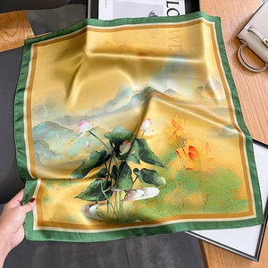 Silk scarf with lotus print and green border on a wooden table with stylish accessories