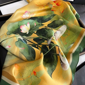 Elegant silk scarf with lotus print in yellow and green, draped on a black tray
