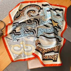 Chic leopard print silk-like square scarf in orange and blue on a wooden table