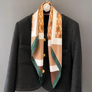 Elegant geometric H-pattern silk scarf paired with a black tweed jacket on grey wall