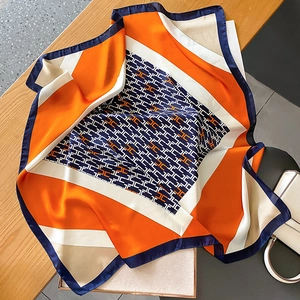 Elegant silk square scarf with geometric pattern draped on a desk with a stylish white bag