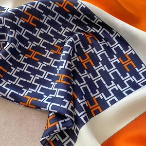 Close-up of silk scarf with H-pattern texture in navy blue and orange draped on fabric